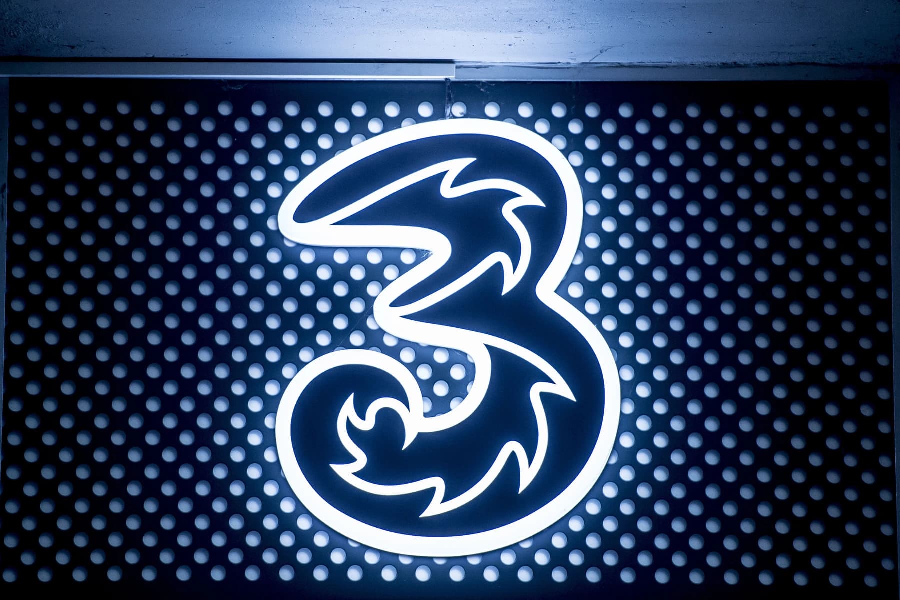 The illuminated 3 symbol against a blue perforated metal wall.